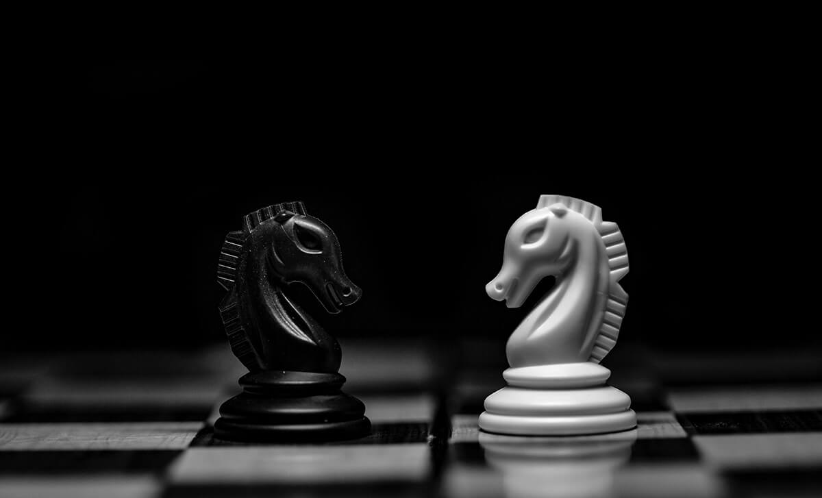 Black horse chess piece facing a white hors chess piece on a chess board